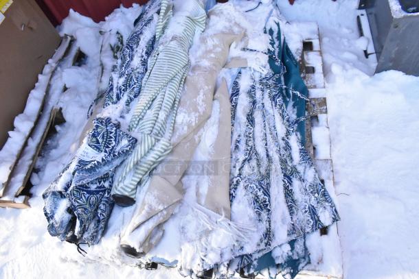 Lot of assorted patio umbrellas in various colors and patterns, snow-covered, on a wooden pallet.