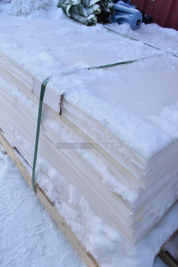 Pallet lot with snow-covered plastic sheets and rolled patio umbrellas, secured with green straps. Items appear used.