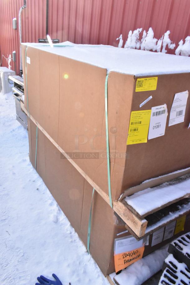 Large cardboard box on a wooden pallet, labeled with QR code and shipping tags. Contains 2 brand new "scratch and dent" items, including a 3-compartment recycling bin. Box is secured with green straps, situated outdoors on snow.