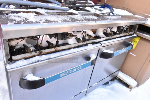 Radiance stainless steel 10-burner range with 2 ovens, over shelf, and backsplash. Visible wear and snow on surface.