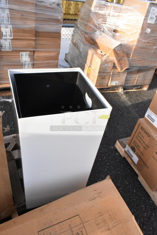 Brand new scratch and dent trash can, white exterior, black interior, visible small dent, packed among pallets.