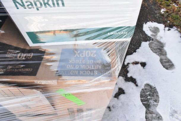 Pallet of wrapped items including napkins, labeled "1,000/CASE." Snowy ground visible, packaging intact.