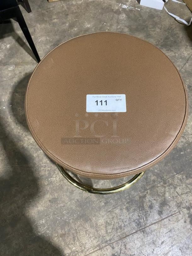 Brand new mid-century modern style brass finish bar stool with tan upholstered seat, round swivel design, auction tag visible.