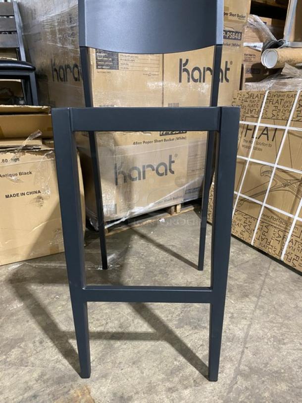 Brand new aluminum black outdoor bar-height stool with light brown imitation teak slat seat; boxes visible in background.