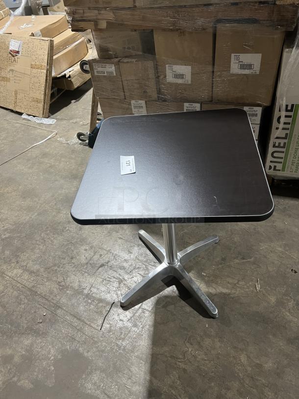 Commercial black square dining table with a modern style, featuring a stainless steel pedestal base. Item tag visible.