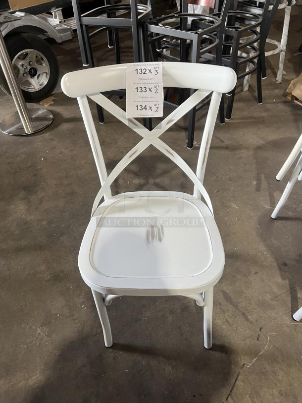 White cross-back stackable dining chair, commercial grade, minor wear on seat, tag numbers 132-134 indicating auction details.