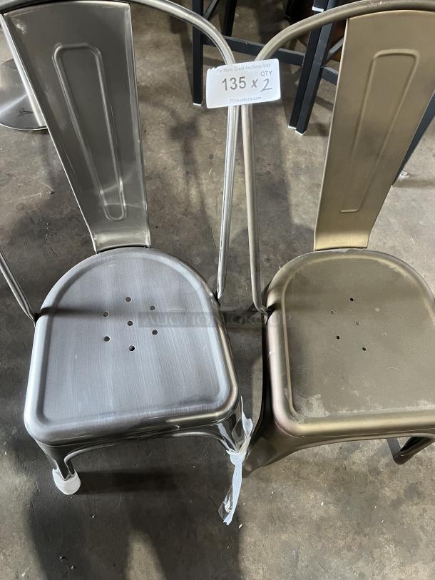Two Tolix-style industrial metal stackable dining chairs, one silver and one copper tone, in used condition with visible wear. Auction label indicates quantity of two, item number 135.