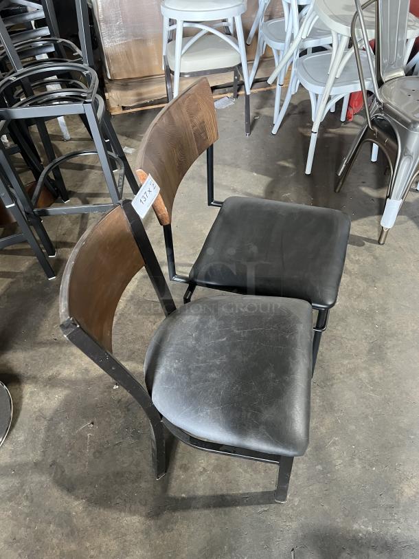 Commercial black stackable dining chair with padded seat, curved wood backrest, and metal frame. Visible wear. Tag reads "13773."