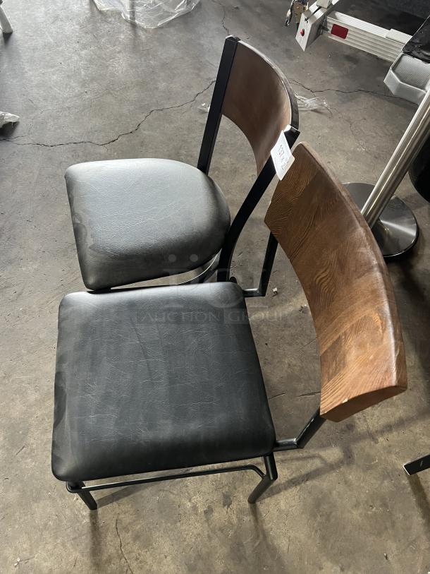 Commercial black padded stackable dining chair with curved wood backrest and metal frame. Good condition; tag visible.