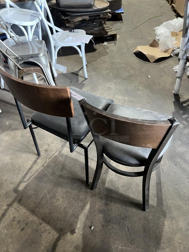 Commercial black padded dining chair with curved wood backrest and metal frame, stackable design, in good condition.