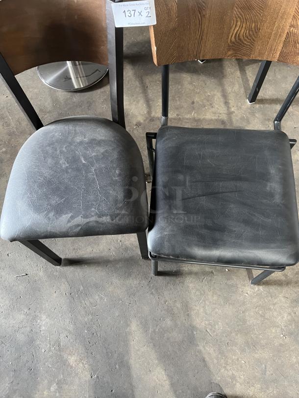 Commercial black padded stackable dining chair with curved wood backrest and metal frame. Shows moderate wear. Tag reads "137 x 2".