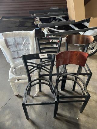 A lot of brand new miscellaneous dining chairs, mix of styles; some wrapped in plastic, metal frames, wooden details, label "141 x 5".