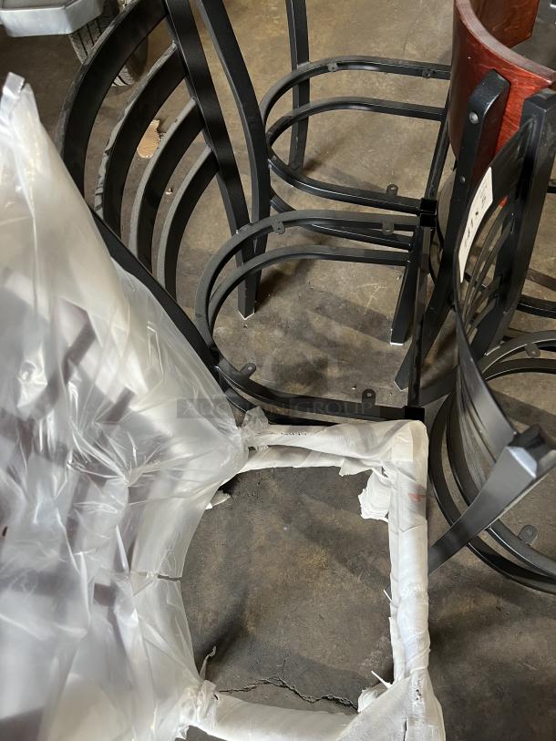 A lot of brand new miscellaneous dining chairs with black metal frames, some partially wrapped in plastic.