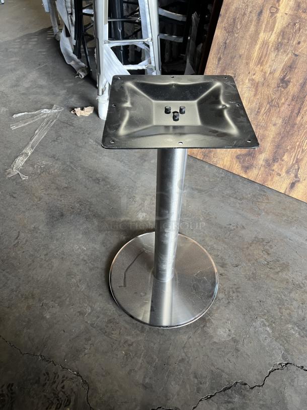 Stainless steel table base with square mounting plate, shown on a concrete floor. Includes wooden multi-style tabletops.