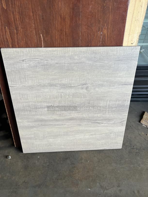 Square wooden tabletop with light wood grain pattern. Part of a stainless steel table base set. Used condition.