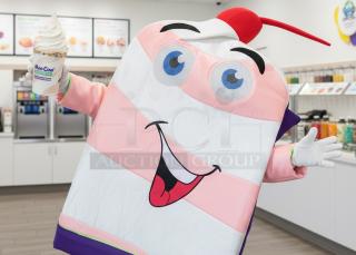 Cheerful cow mascot costume resembling a dessert cup with pink stripes, fun face, cherry, and straw, ideal for promotions.