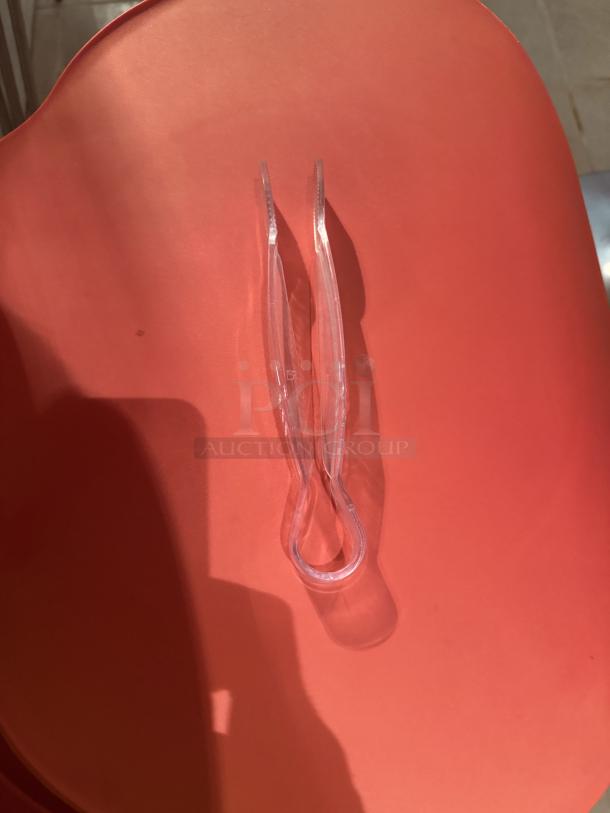 Clear plastic mini serving tong on a red background, durable and lightweight, ideal for parties and events.