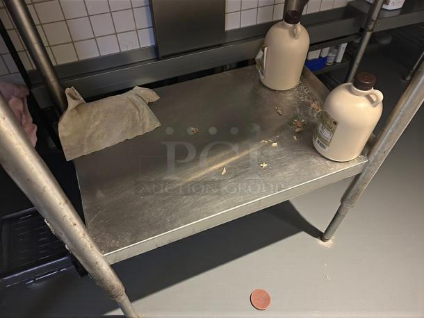 Omniteam stainless steel 24"x35" worktable with backsplash, sturdy, used condition, visible wear and items on surface.