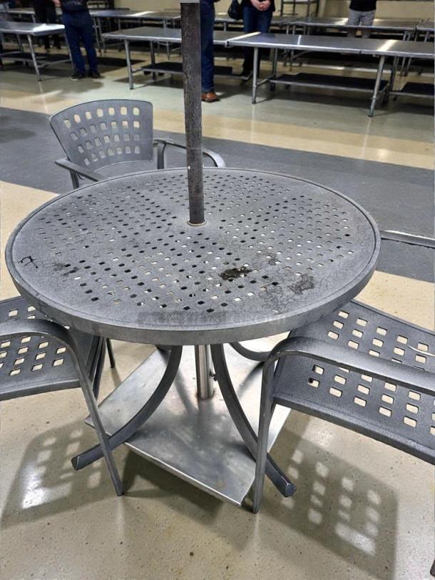 Pristine round metal patio table, commercial grade, umbrella-ready, with four perforated chairs, fully inspected for outdoor use.