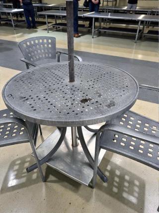 Pristine round metal patio table, commercial grade, umbrella-ready, with four perforated chairs, fully inspected for outdoor use.