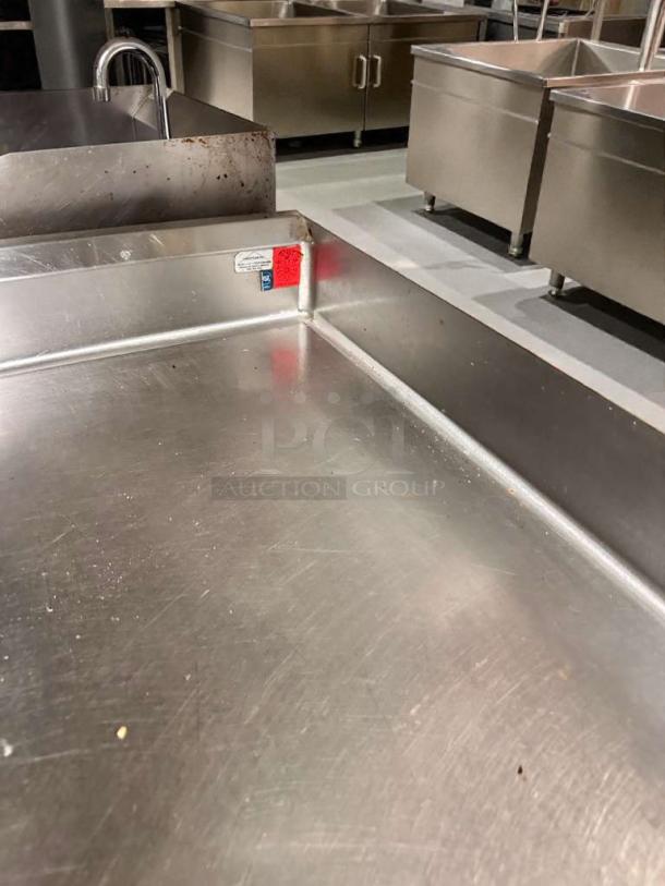 Pristine commercial stainless steel work table with backsplash, fully cleaned, ready for use. Features a durability tag.