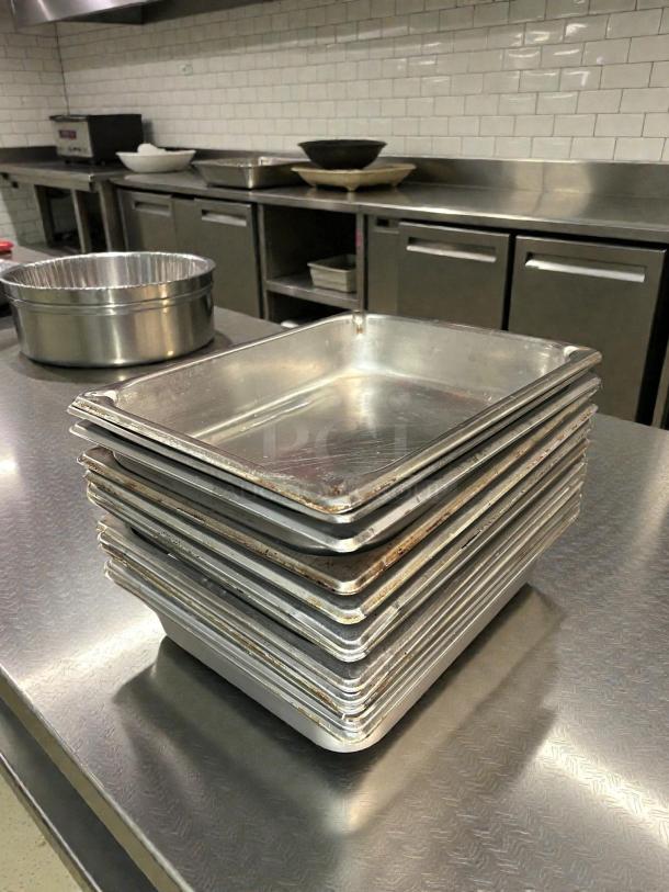 Stack of Vollrath 30222 Super Pan V® Half Size Steam Pans, stainless steel, showing minor wear, set on a commercial kitchen counter.
