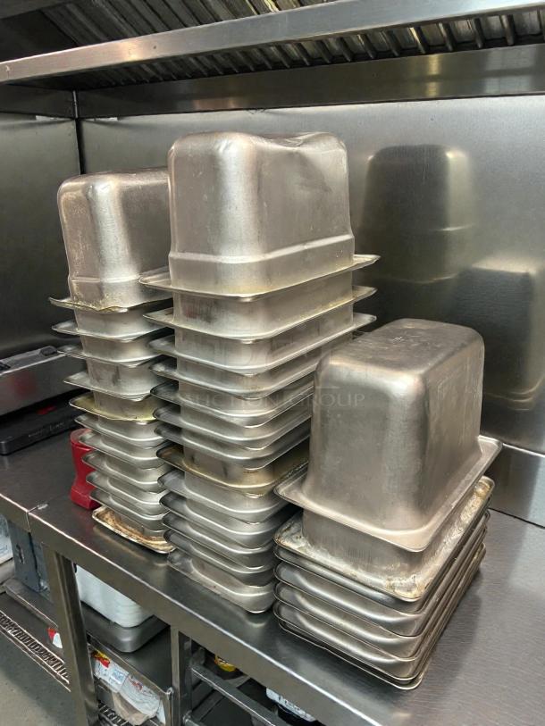 Stacks of Winco SPJH-904 solid steam table pans, 1/9 size, heavy weight, in amazing condition on a steel surface.
