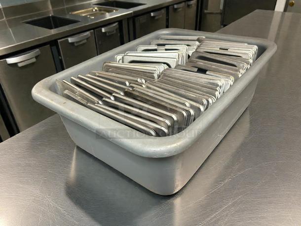 Winco SPCS 1/6 size stainless steel slotted steam table pan covers in excellent condition, stacked in a gray bin.