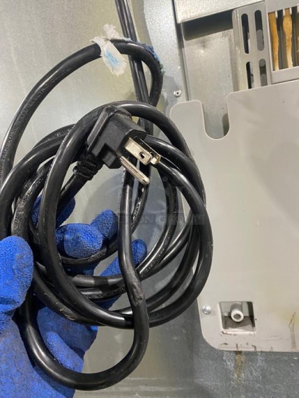 Coiled power cord for Atosa MBF8002GR freezer, inspected by gloved hand, showing standard plug and wiring detail.