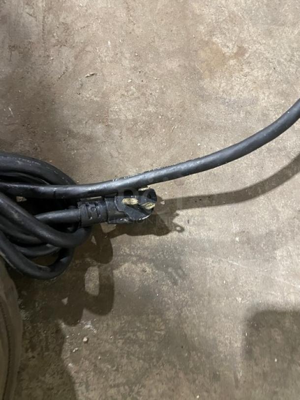 A black power cable and plug on a concrete floor, part of the Imbera Elite Series Commercial Merchandiser.