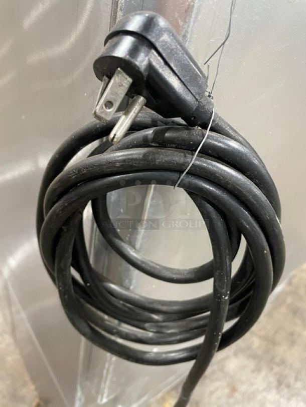 Coiled black power cord with a standard three-prong plug, attached to stainless steel appliance.