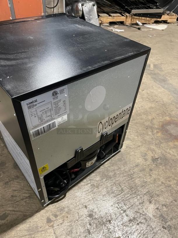 Schmecke Commercial black wine cooler, single glass door, 12-bottle capacity with chrome wire rack. Model label visible. 115V.