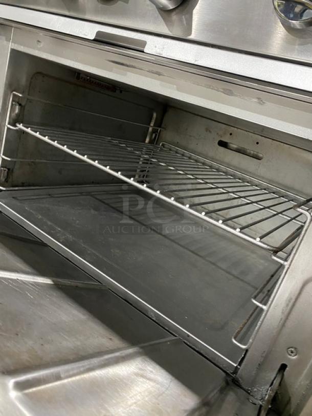 Qualite commercial stainless steel gas range/oven with 6 burners, backsplash, overhead salamander shelf, and wired oven rack.