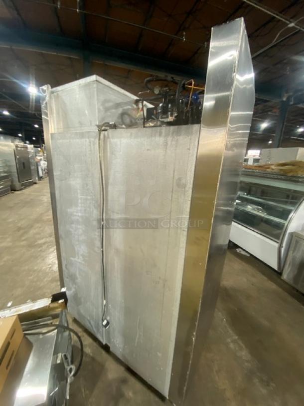 Traulsen stainless steel 4 half-door commercial refrigerator with built-in pan slides, on legs, visible in a warehouse setting.