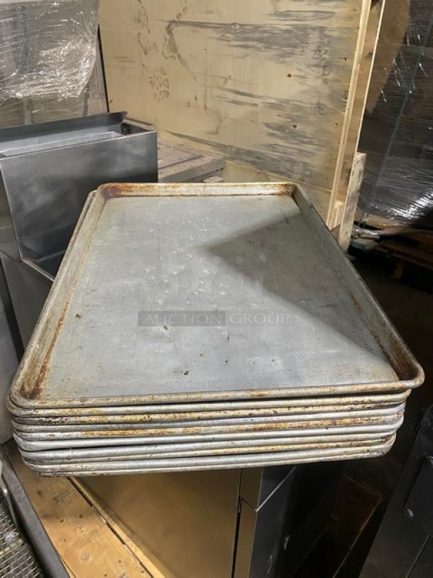 Stack of commercial rectangular baking sheet pans in used condition, showing signs of wear and rust. Suitable for bulk bidding.