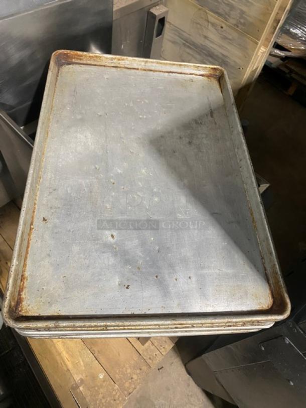 Commercial rectangular baking sheet pan, stack of four, metal, used condition, some wear and rust visible on edges.