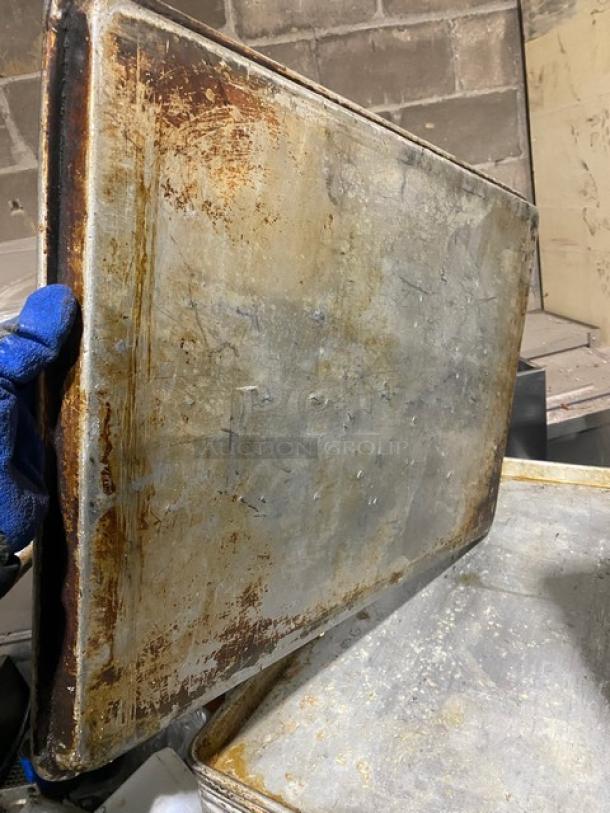 Commercial rectangular baking sheet pan with visible wear and rust, held vertically. Used condition.