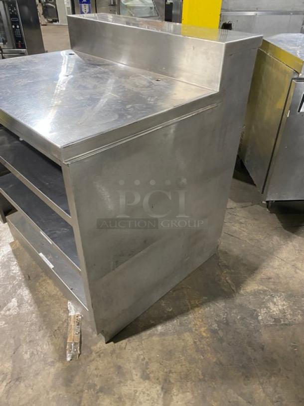 Commercial stainless steel multi-tier dry worktop table with enclosed cabinet, rear shelving, and backsplash. Used condition.