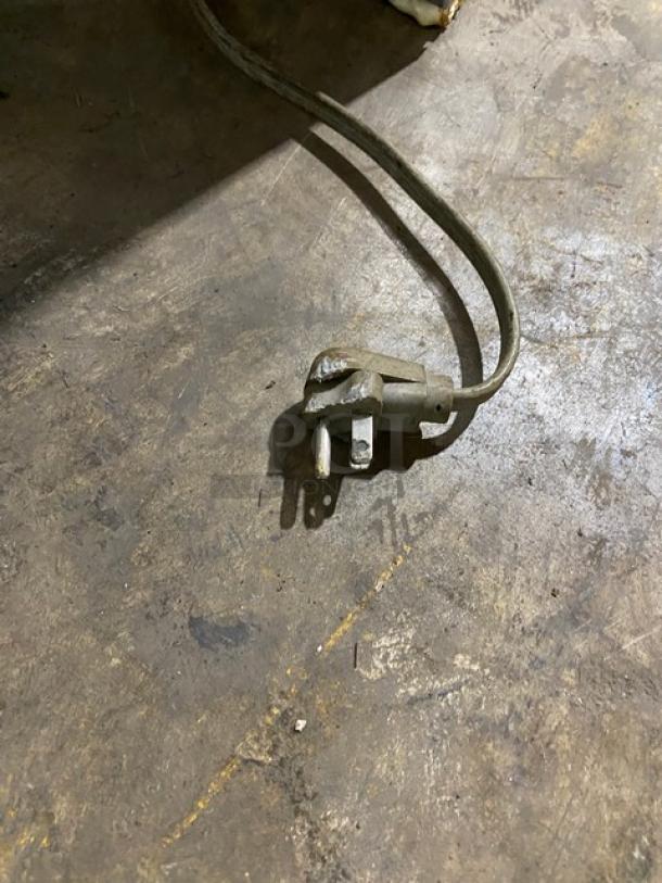 Commercial bakery display showcase power cord on concrete floor, showing wear and some dirt.