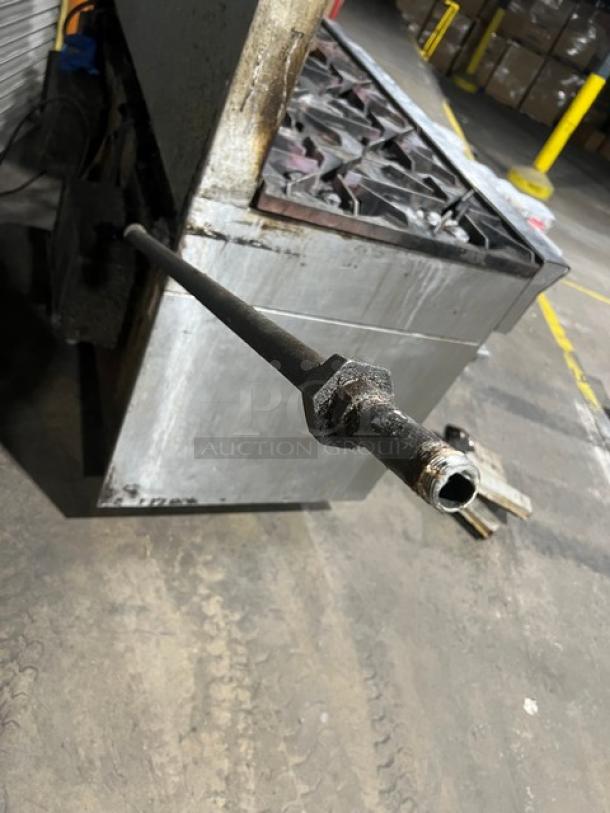U.S. Range stainless steel 10-burner gas range with double oven, backsplash, and wired oven rack. Industrial setting. Signs of use.