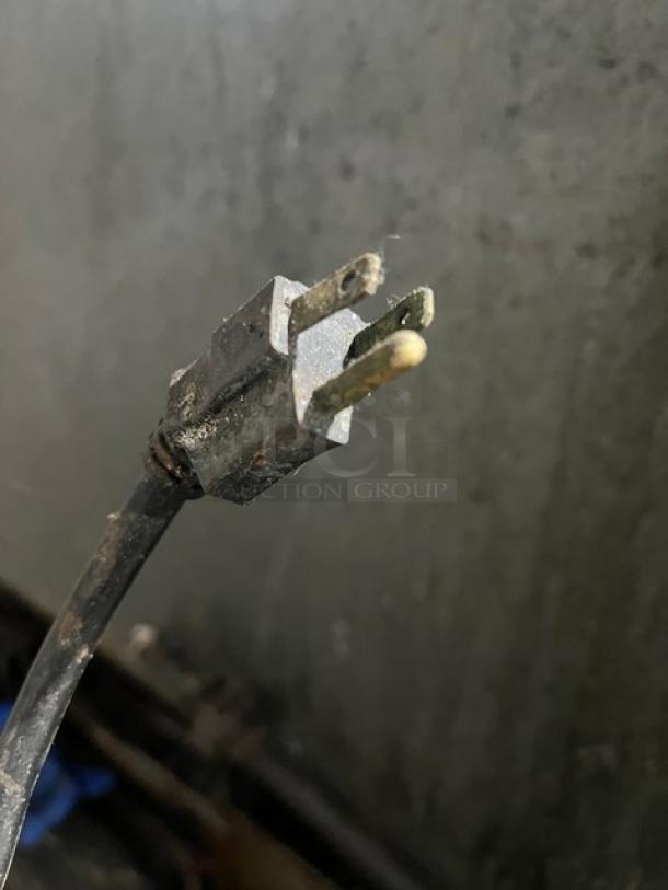 A close-up of a worn power plug showing two metal prongs, likely part of the U.S. Range gas-powered 10-burner range.