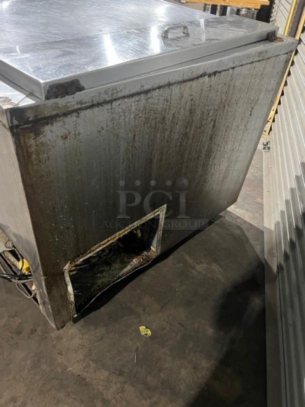Commercial stainless steel refrigerated prep table with visible wear and rust. Features a poly-coated wired rack and casters.