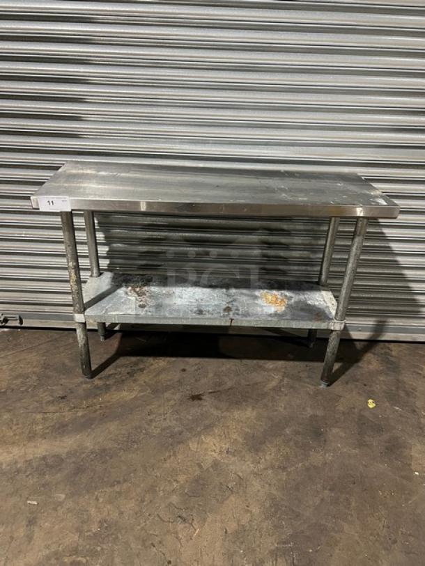 Commercial stainless steel worktop table with single undershelf, on legs. Visible wear and marks indicating use.
