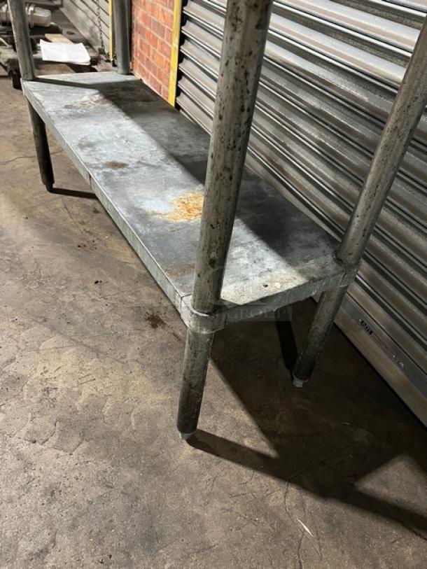 Commercial stainless steel worktop table with single undershelf, on legs, showing signs of rust and wear.