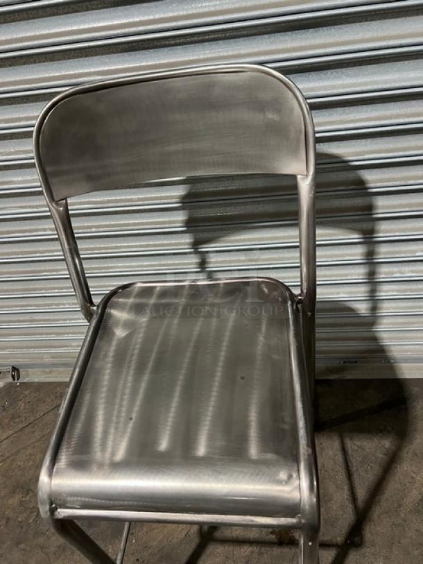 Commercial stackable bar-height chair, metal, sturdy construction, slightly worn, ideal for bar or restaurant use.