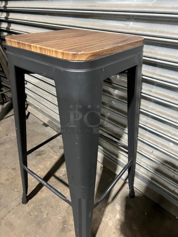 Commercial black stackable bar-height stool with wooden seat and metal frame, in good condition.