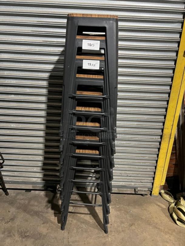 Stack of commercial black stackable bar-height stools, metal frame, wooden seat, labeled 18.5" and 19.5".