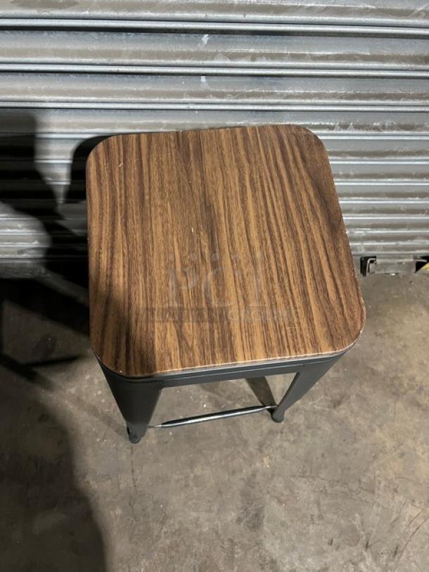 Commercial black bar-height stool, stackable, wooden seat, metal legs, durable condition, suitable for bars and restaurants.