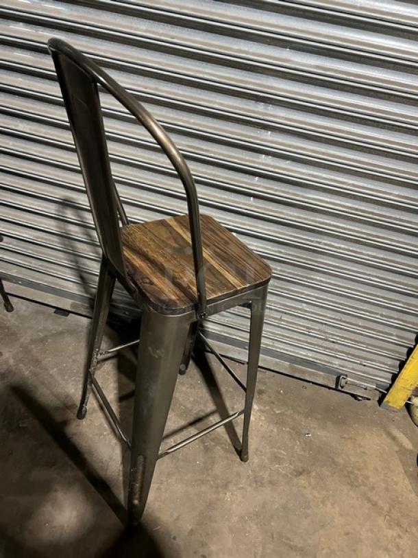 Commercial stackable bar-height chair with a metal frame and wooden seat. Durable design, suitable for high-traffic use.