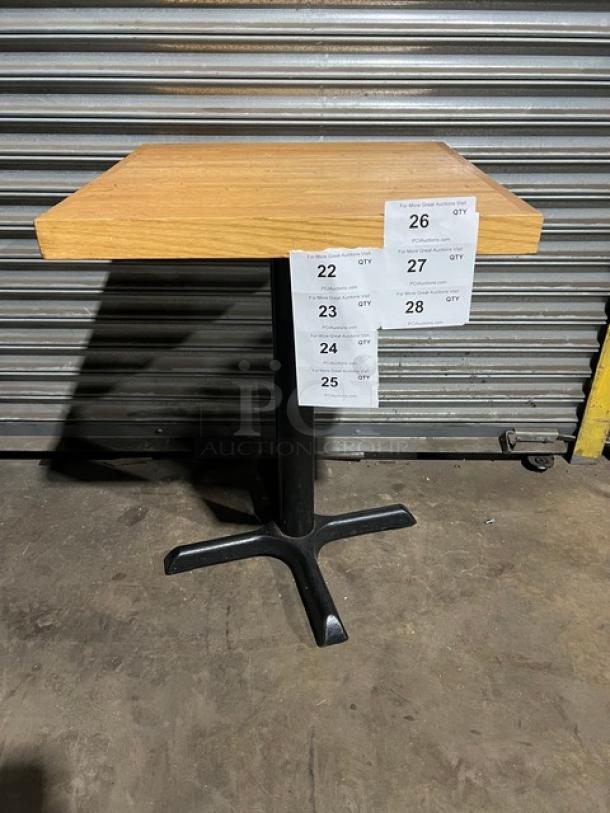 Commercial dining-height table with a wood top and black metal pedestal base. Condition appears good. Auction tags visible.